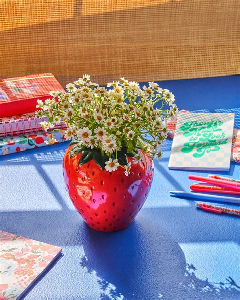 A Red Vase Filled With White Flowers Sitting On Top Of A Blue Table