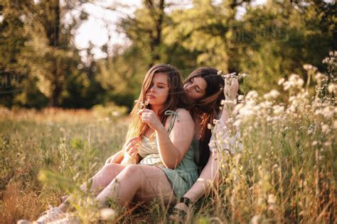 Lesbian Couple Sitting In Field Of Flowers In Forest During Summer Stock Photo Dissolve