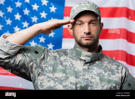 Patriotic Military Man In Uniform And Cap Giving Salute Near American
