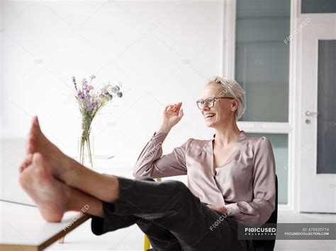Smiling Businesswoman With Feet On Desk Relaxing In Loft Office