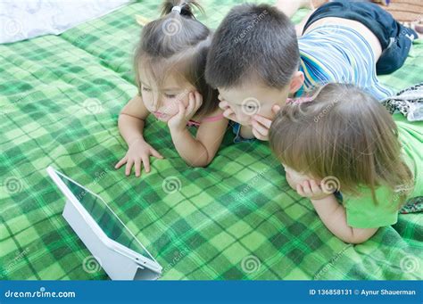 Three Kids Looking On Tablet Lying On Bed At Home Children Time