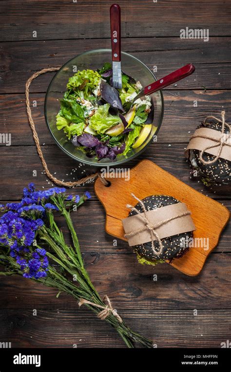 Delicious Black Burgers Salad And Blue Flowers On Dark Wood Table