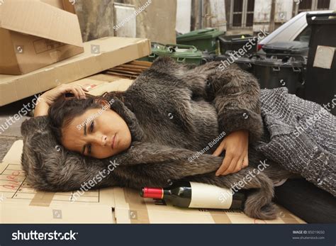 Young Hobo Woman Lying On City Pavement With Bottle Of Wine Stock Photo