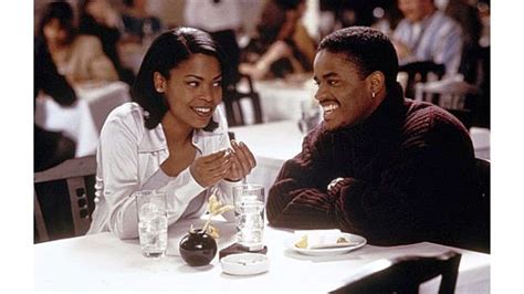 A Man And Woman Sitting At A Table With Glasses In Front Of Them Smiling