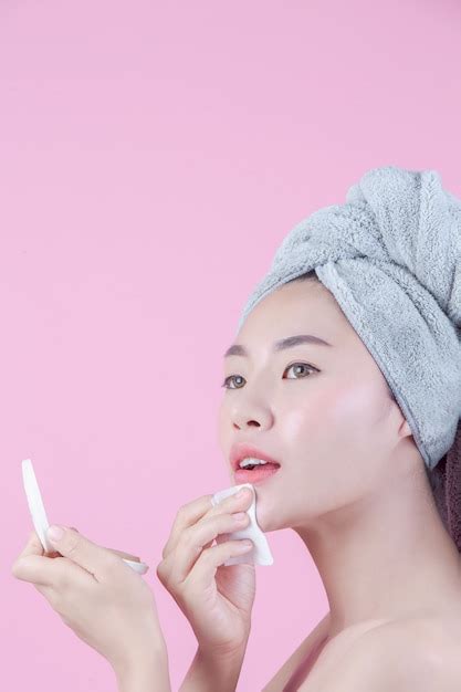Asiatische schöne frau säubert das gesicht auf einem rosafarbenen hintergrund Kostenlose Foto