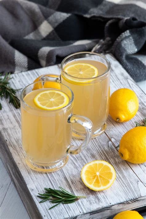 Two Mugs Filled With Lemonade Sitting On Top Of A Wooden Cutting Board