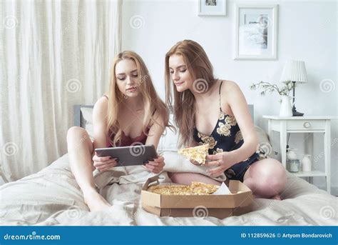 Two Happy Girls In Pajamas Spending Time Together At Bachelorette Party And Eating Pizza In Bed