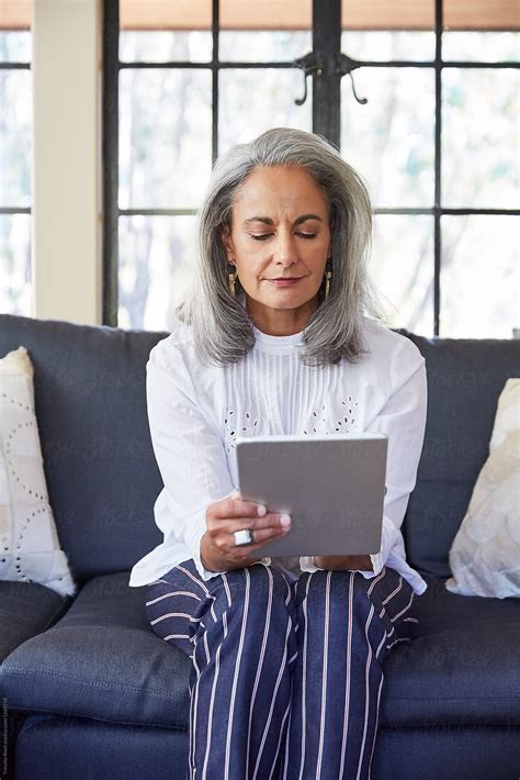 Mature Woman With Grey Hair Using A Digital Tablet In Living Room By Stocksy Contributor