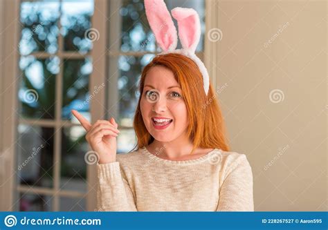 redhead woman wearing easter rabbit ears at home very happy pointing with hand and finger to the