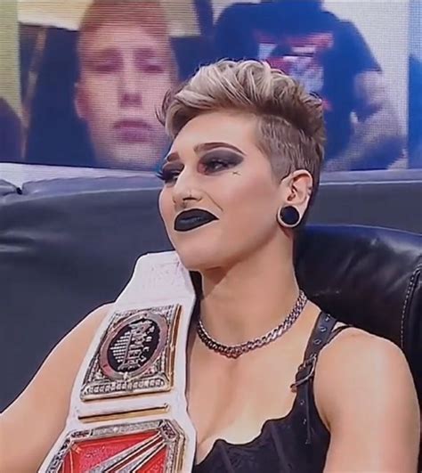 A Woman Sitting In A Chair With A Wrestling Belt On Her Chest And Black