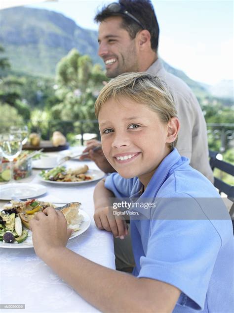 Portrait Of A Young Boy Sitting At A Meal On A Table Outdoors High Res