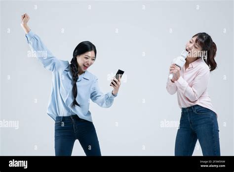 Two Asian Women Sisters Singing With Wireless Mic And Mobile Karaoke Application On Phone Stock