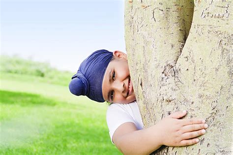 Happy Little Boy Hiding Behind Tree In Park Playing Hide And Seek