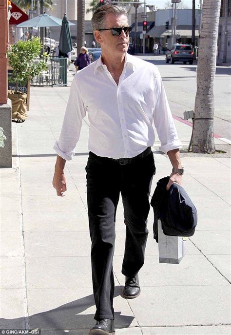 60 year old pierce brosnan carries his jacket like a gentleman as he walks on the streets of
