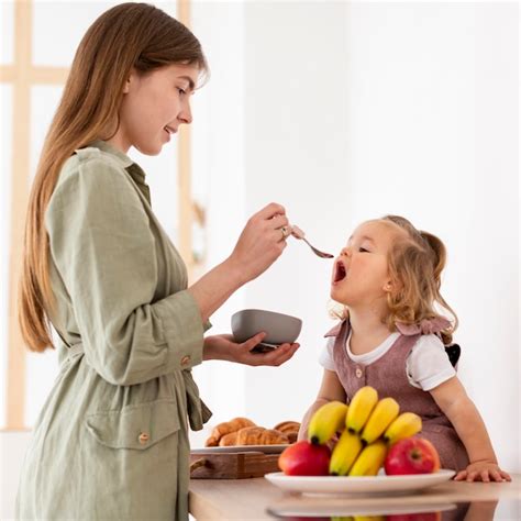 Madre Sonriente Que Alimenta A La Hija Foto Gratis