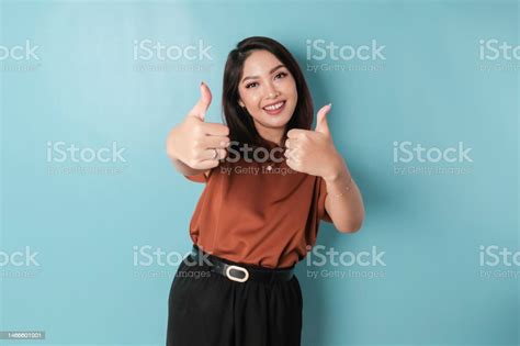 Excited Asian Woman Gives Thumbs Up Hand Gesture Of Approval Isolated By Blue Background Stock
