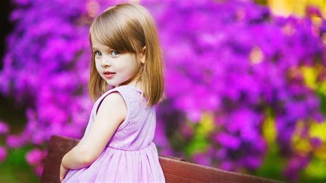 Cute Little Girl Is Standing In Dark Purple Flowers Background Wearing