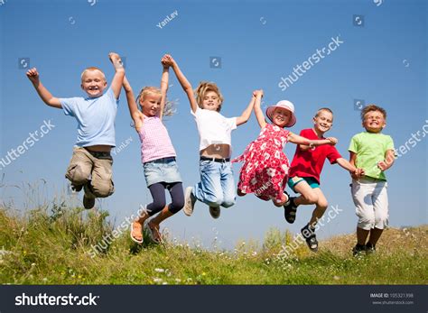 Group Happy Children Jumping On Summer Meadow Against Blue Sky Stock