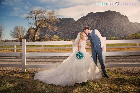 A Bride And Groom Kissing In Front Of A White Fence With Mountains