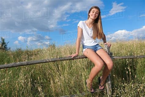 Teenage girl sitting on wooden fence, Tuscany, Italy - Stock Photo - Dissolve