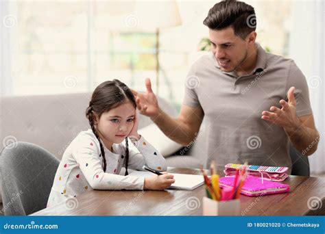 Father Scolding His Daughter While Helping With Homework At Table Stock