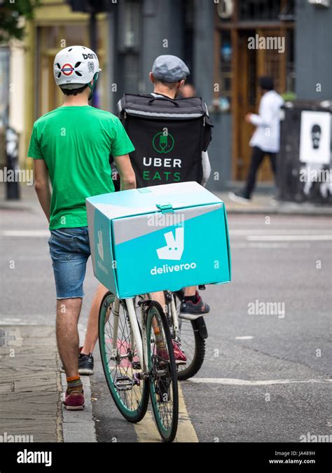 Deliveroo And Uber Eats Food Delivery Bike Couriers Wait At Traffic Lights While Delivering Food