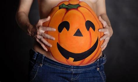 A Pregnant Woman Holding A Pumpkin Painted On Her Stomach With Both Hands And The Belly