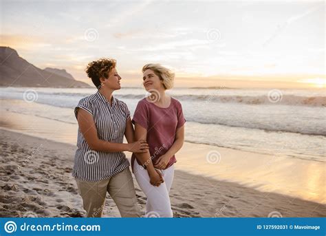 smiling lesbian couple enjoying a romantic walk along a beach stock