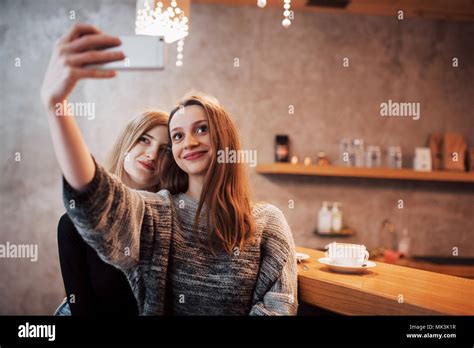 two friends drinking coffee in a cafe taking selfies with a smart phone and having fun making