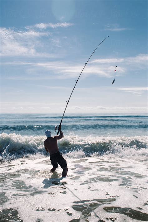 Man Casting Large Fishing Rod In Ocean Surf By Stocksy Contributor