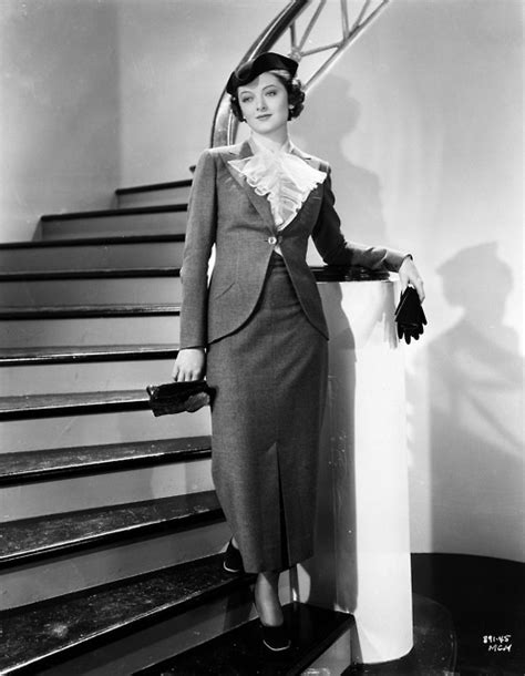 An Old Photo Of A Woman In A Suit And Hat Standing Next To Some Stairs