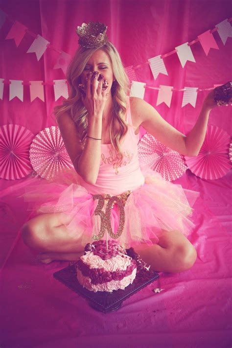 A Woman Sitting On A Bed With A Cake In Front Of Her And Pink Decorations Behind Her