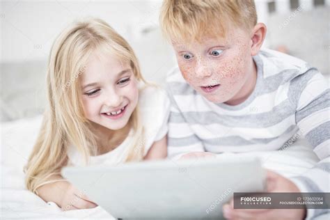 Brother And Sister Lying In Bed And Using Tablet — Siblings Cheerful