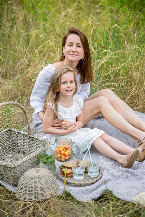 Красивая молодая мать и ее маленькая дочь в белом платье имея потеху в пикнике Они сидят на