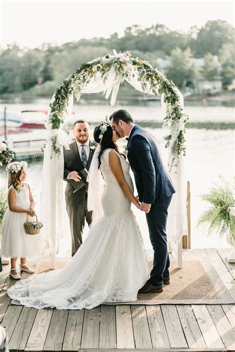 A Bride And Groom Kiss As They Stand On A Dock With Their Wedding Party