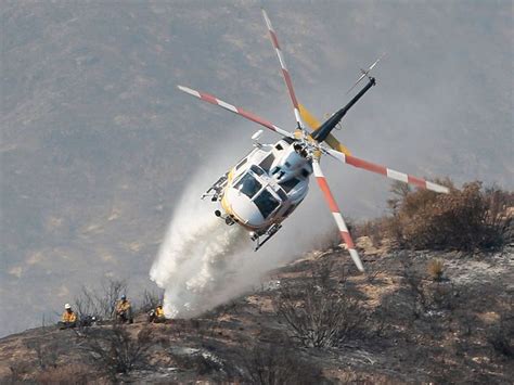 A Ground Crew Watches As A Firefighting Helicopter Drops Water On A