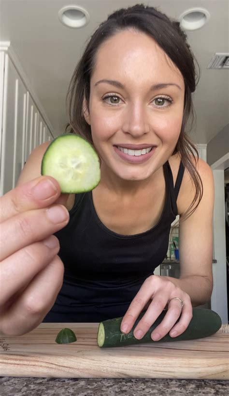 A Woman Holding A Cucumber In Her Right Hand And Smiling At The Camera