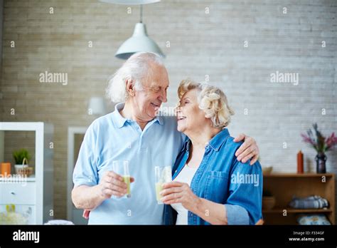 senior husband and wife holding glasses with healthy homemade fruit drink and looking at one