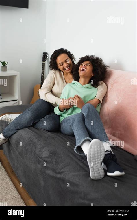 Happy African American Mother Tickling Cheerful Preteen Daughter In Living Roomstock Image