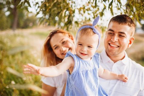 Happy Mom And Dad Hold Little Daughter On Their Arms Standing In The
