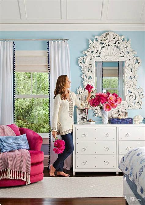 A Woman Standing In Front Of A Mirror Next To A Dresser With Flowers On It