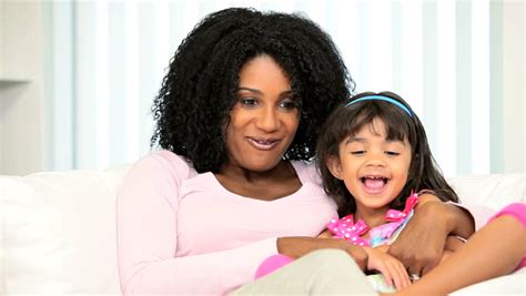 Beautiful Young Ethnic Mother Tickling Her Giggling Pre School Daughter On Home Couch Stock