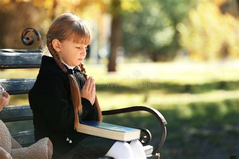 Little Girl With Bible Praying On Bench Outdoors Stock