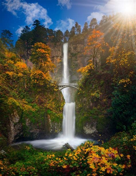 The Sun Shines Brightly Over A Waterfall With Fall Foliage Surrounding