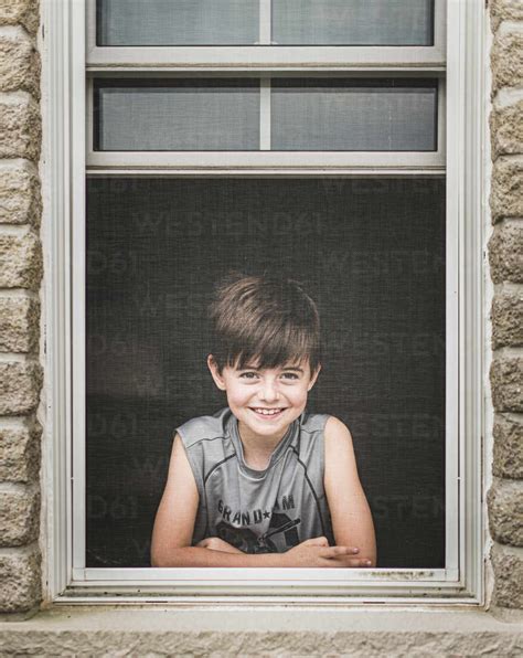 Young Boy Looking Out Through The Screen Of An Open Window Stock Photo