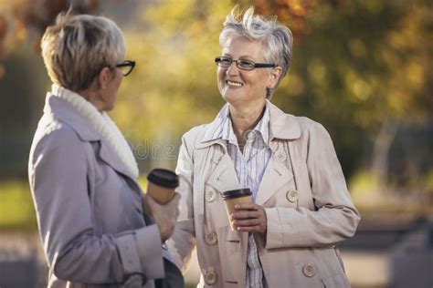 Senior Women Or Friends Drinking Coffee Walking Along Park Stock Image