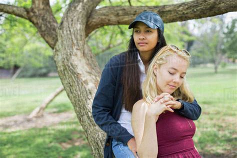 Young Lesbian Couple Sitting Against Tree Trunk At Park
