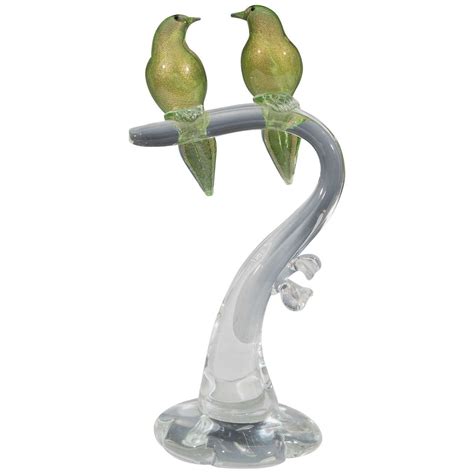 Two Green Birds Perched On A Branch With Clear Glass Base And Silver Colored Metal Stem
