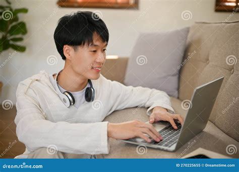 Chilling Asian Man Using Laptop On A Sofa In His Living Room Stock