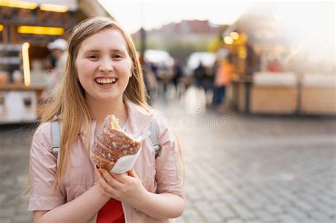 Portrait Of Happy Modern Girl At Fair In City Eating Trdelnik Stock